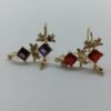 Aretes Patlajtli. Laminado de oro con diseño de alas y piedras cuadradas rojas/moradas.