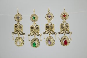 Aretes Moño de Escaramuza Aretes Moño de Escaramuza. Laminado de oro, diseño largo con moño, filigrana, perlas y gemas de colores.