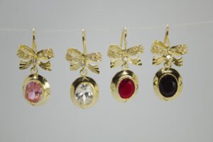 Aretes Nudo de Gala Aretes Nudo de Gala. Laminado de oro, moño brillante y gema ovalada de color (rosa, transparente, rojo, negro).