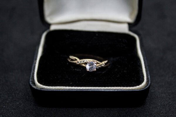 Anillo Artesanal Abrazo de Cristal. Oro 10K (aprox. 2.1 gr). Diseño entrelazado con circonias y cristal central. Producto Artesanal. (Entrega: 5-7 días hábiles)